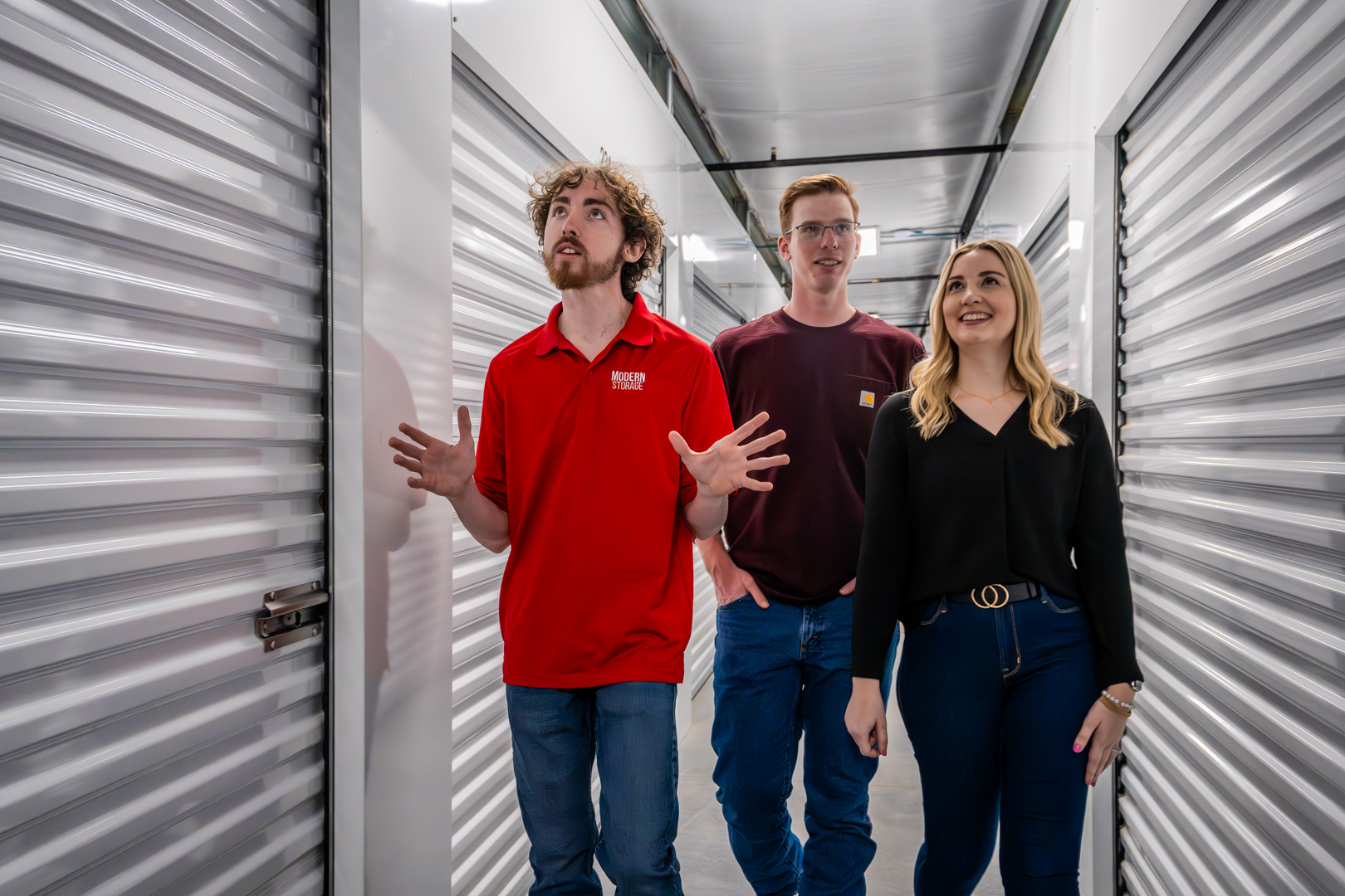 Modern Storage® Shackleford team member giving a tour to two tenants inside a brightly lit, climate-controlled hallway lined with white roll-up doors